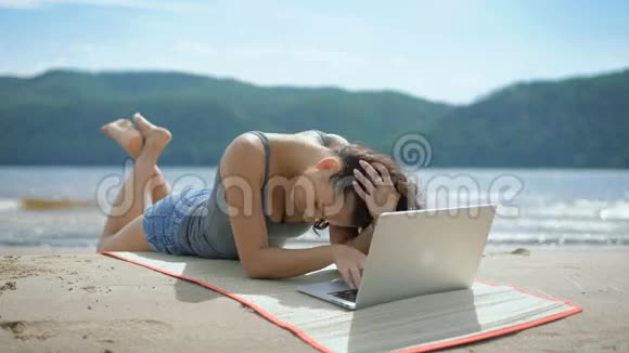 一位年轻漂亮体贴的女士正在沙滩上用笔记本电脑躺着汤米视频的预览图