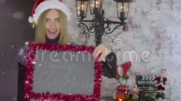 美丽的金发圣诞女孩手里拿着黑板上写着圣诞快乐视频的预览图