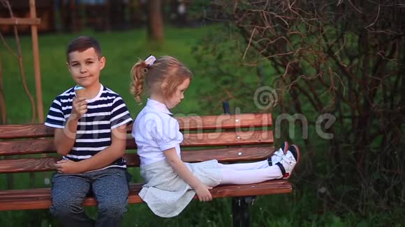 男孩吃冰淇淋坐在长凳上而女孩正在看视频的预览图
