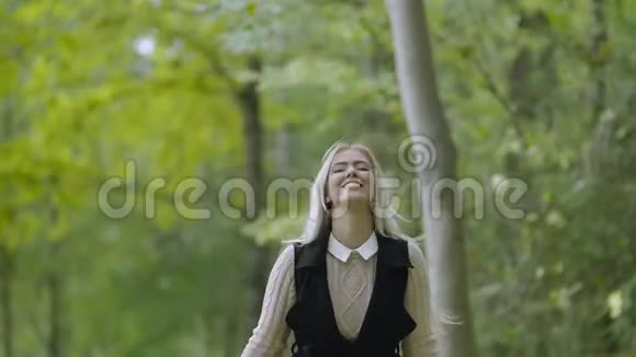 美丽的微笑的年轻女子走在公园里吐出秋天的枫叶视频的预览图