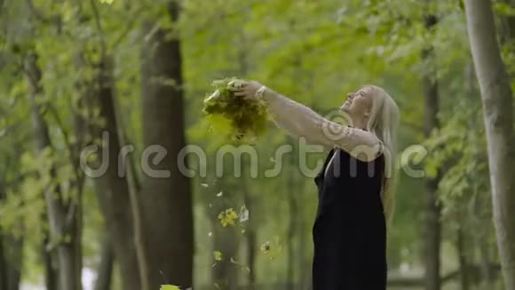 美丽的微笑的年轻女子走在公园里吐出秋天的枫叶视频的预览图