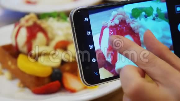 特写镜头女性双手在智能手机上拍摄一张维也纳华夫饼冰淇淋和新鲜水果甜点的照片视频的预览图