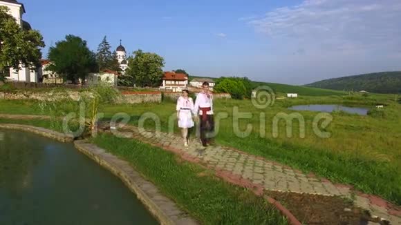 婚礼当天新娘和新郎沿着湖边散步的空中景色新婚夫妇穿着传统西装视频的预览图