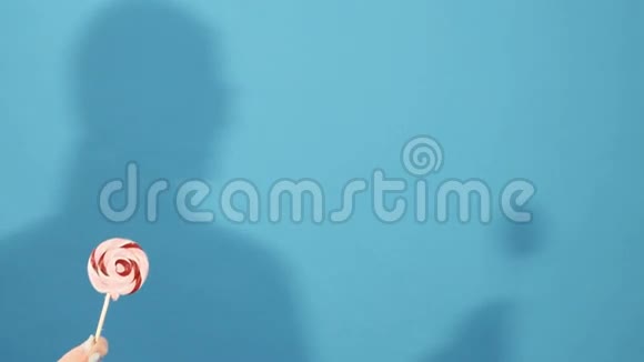 女性手拿着五颜六色的棒棒糖在蓝色背景与女孩阴影在工作室视频的预览图