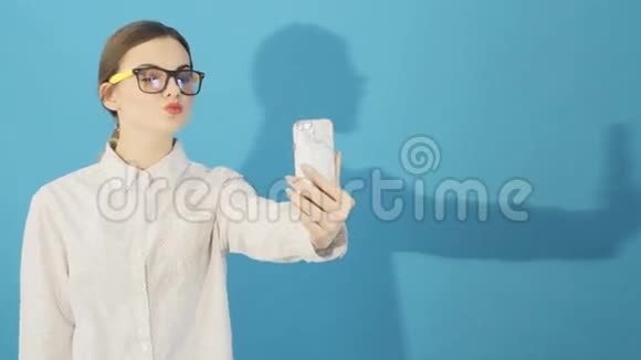 布鲁内特正在使用智能手机在蓝底工作室穿着时尚的迷人的嬉皮士女孩视频的预览图