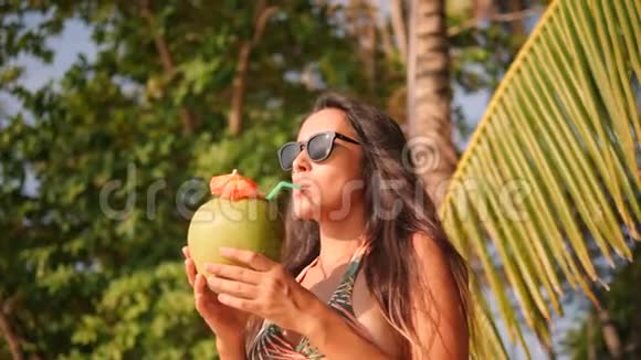 迷人的混合种族年轻旅游妇女在热带海滩喝新鲜泰国椰子水鸡尾酒4K慢动作视频的预览图