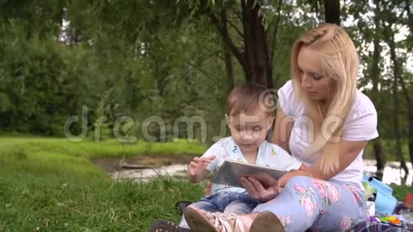快乐的母亲和她的小儿子在公园里玩平板电脑视频的预览图