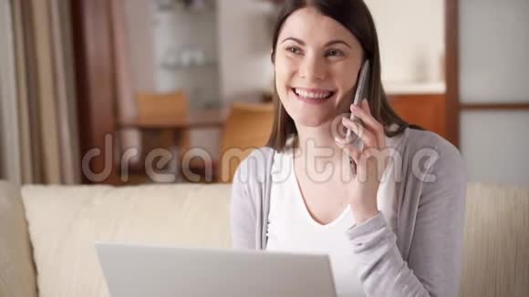 忙碌的女人坐在家里拿着笔记本电脑和智能手机通过手机在屏幕上讨论项目视频的预览图
