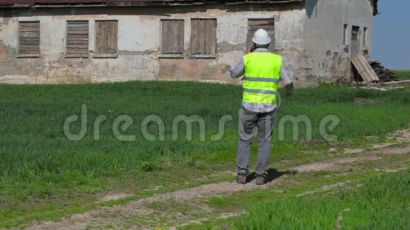 建筑检查员在草地上废弃的损坏的房子附近用智能手机交谈视频的预览图