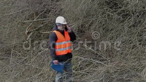Lumberjack用智能手机聊天在一堆树枝附近散步视频的预览图