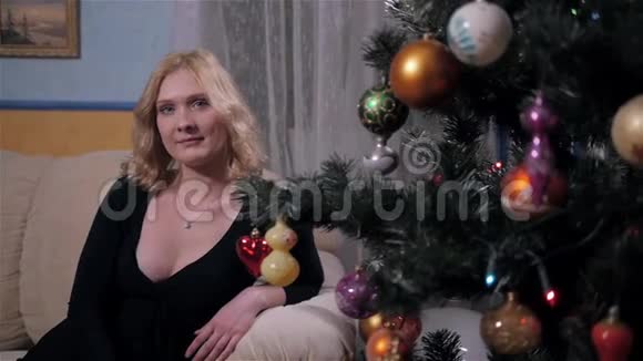 家中圣诞树旁有金发的漂亮年轻女子视频的预览图