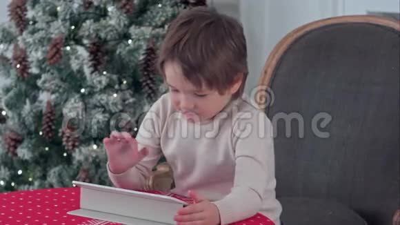 严肃的小男孩坐在椅子上在圣诞节期间使用平板电脑视频的预览图