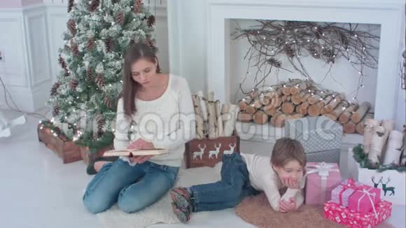 妈妈在圣诞树旁为她的小儿子读一本书视频的预览图