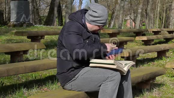 使用平板电脑和在公园的长椅上看书的人视频的预览图