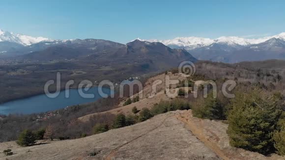 空中飞行无人驾驶飞机飞越森林山谷湖泊鸟瞰阿尔卑斯山白雪覆盖的山脉晴空万里视频的预览图