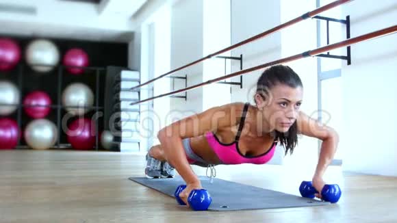 健身房里的布鲁内特女士用哑铃做俯卧撑锻炼视频的预览图