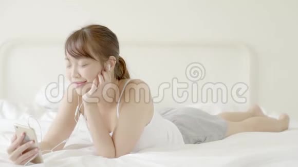 美丽的肖像年轻的亚洲女人躺着快乐的耳机听音乐放松和享受在卧室里视频的预览图