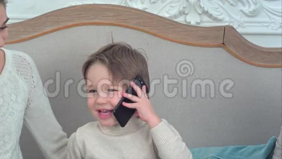 微笑的小男孩在电话里交谈周围是他幸福的家庭视频的预览图