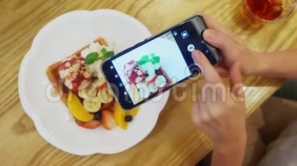 特写镜头女性双手在智能手机上拍摄一张维也纳华夫饼冰淇淋和新鲜水果甜点的照片视频的预览图