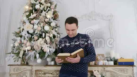 穿着针织毛衣的年轻人在圣诞树旁看书视频的预览图