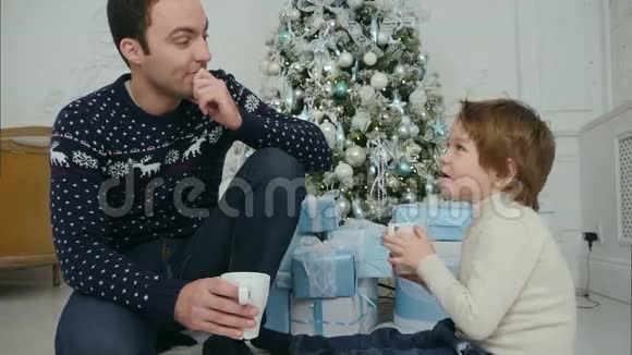 快乐的爸爸和儿子在家中的圣诞树旁喝茶聊天视频的预览图