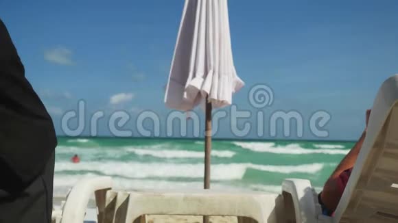 一个面目全非的侍者端着椰子鸡尾酒在海边让年轻人放松3840x2160视频的预览图