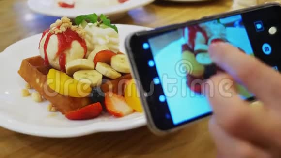特写镜头女性双手在智能手机上拍摄一张维也纳华夫饼冰淇淋和新鲜水果甜点的照片视频的预览图