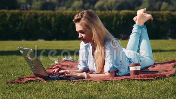 年轻女子拿着笔记本电脑在草地上放松视频的预览图