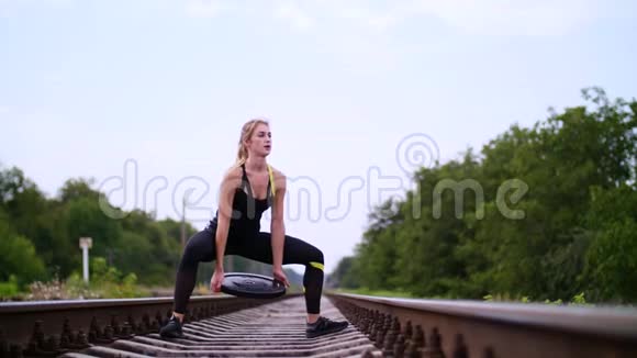 美丽的运动年轻的金发女人穿着黑色的紧身裤用一个沉重的盘子做运动在上面视频的预览图