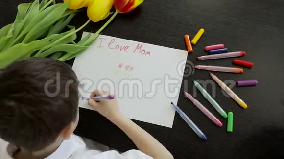 快乐的小男孩在桌子上为他妈妈做了一张节日卡片视频的预览图