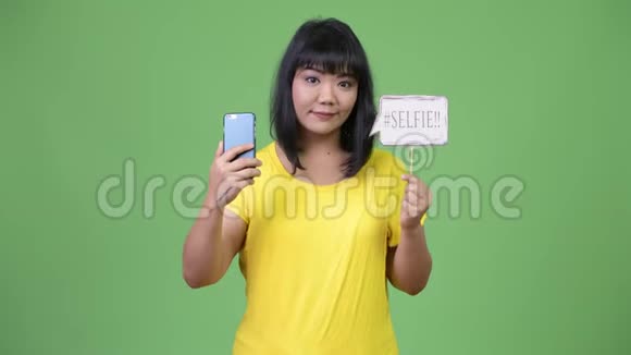 美丽快乐的亚洲女人拿着手机和自拍纸标志视频的预览图
