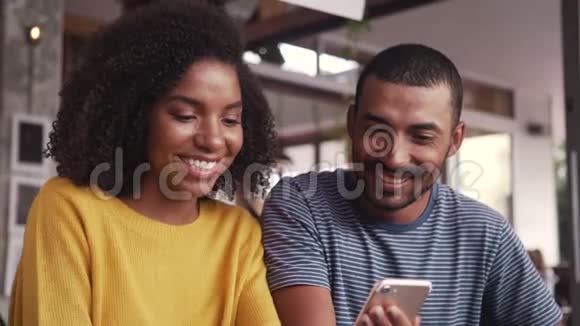 快乐的年轻夫妇在咖啡馆里看手机视频的预览图