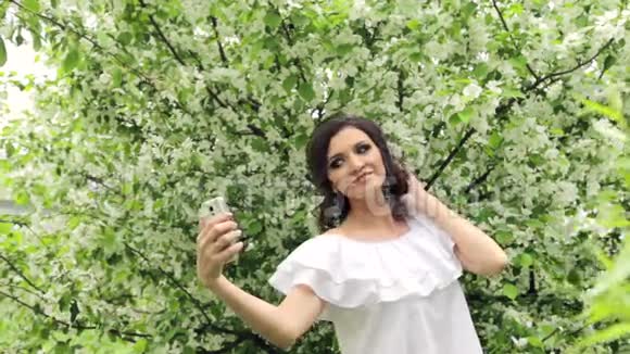 快乐的女人在盛开的花园里的智能手机上自拍视频的预览图