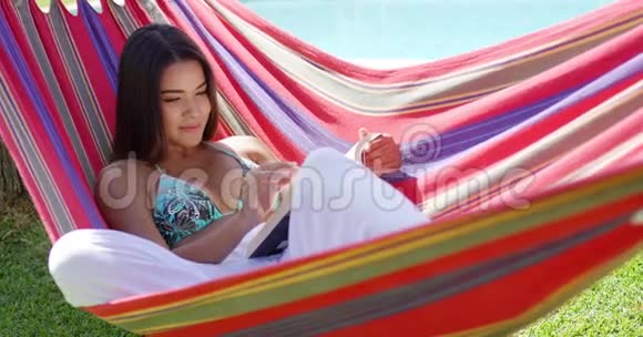 坐在吊床上带书的轻松女人视频的预览图