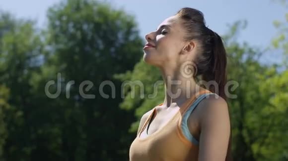 阳光明媚的一天年轻的黑发女人在公园跑步后喘口气视频的预览图
