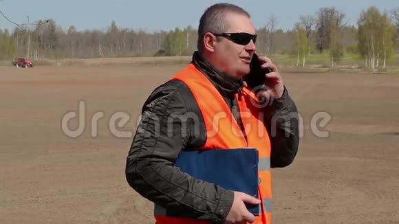 农夫在拖拉机耙地的田里用智能手机说话视频的预览图