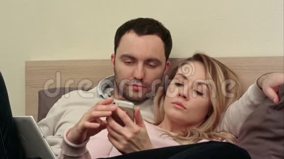 美丽的一对夫妇坐在床上在智能手机上看着旅行中的照片触摸着屏幕视频的预览图