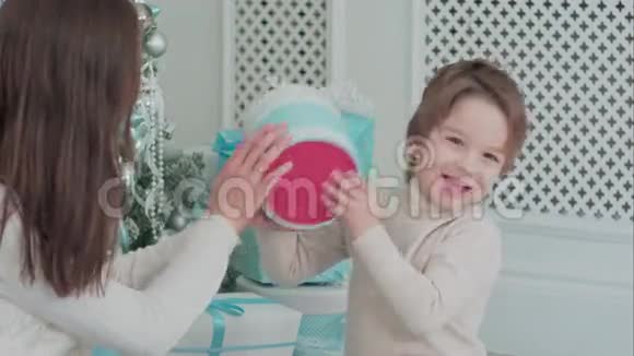 坐在圣诞树旁的母亲和幸福的儿子正在检查礼物视频的预览图