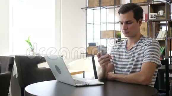 男人在手机上说话的肖像坐在办公桌前看着笔记本电脑视频的预览图