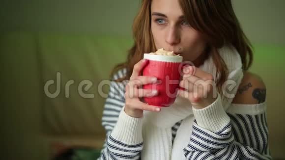戴着围巾的年轻女人喝着红色杯子里的咖啡视频的预览图
