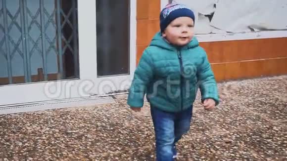 一个穿夹克的小男孩沿着院子里的小路跑慢动作视频的预览图