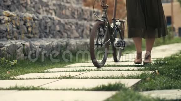 女人的腿在城市道路上骑自行车旁行走女子脚和自行车轮视频的预览图