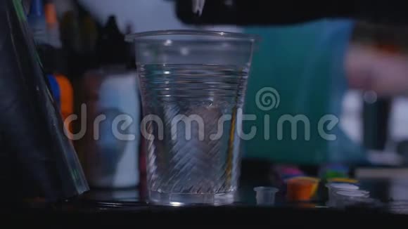 一个纹身师在纹身工作室里慢动作地在一杯水中混合墨水视频的预览图