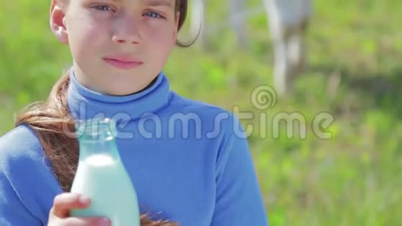 一个男孩在草地上拿着一瓶牛奶的肖像一个男孩在田里的奶牛旁边喝牛奶健康的生活方式视频的预览图