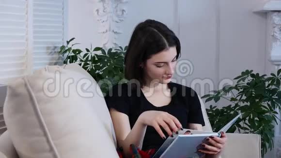 漂亮的年轻女人躺在沙发上看书视频的预览图