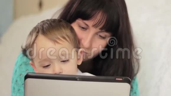 妈妈和孩子坐在沙发上看着平板电脑的展示视频的预览图