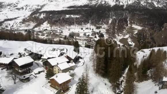 冬季空中无人驾驶飞机在冰雪覆盖的小镇和森林森林山谷中建立起来高山自然中的雪视频的预览图