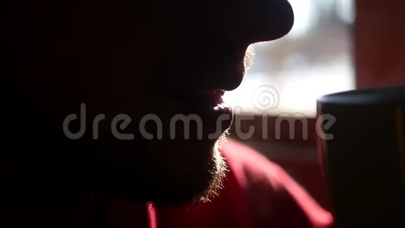 一个留着红胡子的男人喝着背景窗上的蒸汽热茶特写慢动作视频的预览图
