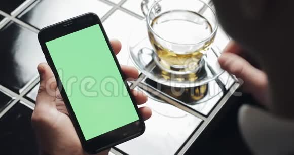 年轻的商人使用带有绿色屏幕触摸板的smarthpone并在咖啡馆打手势接近一个拿着手机的家伙敲视频的预览图