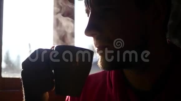 一个留着短胡须的人坐在阳光下的窗前喝着一杯热咖啡享受着这种味道视频的预览图